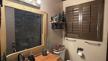A bathroom with a wooden vanity, a mirror with lights, a toilet, and a window with shutters.
