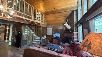 A spacious living area with a high ceiling, a fireplace, a television, and a large window.