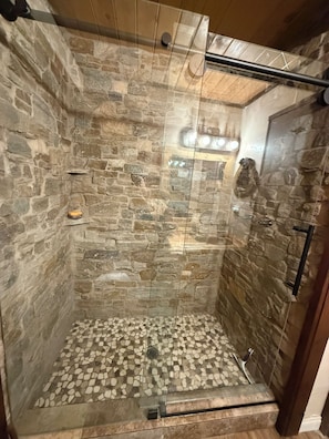 A shower with stone walls and a mosaic floor.