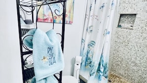 A bathroom with a shower, a toilet, a towel rack with towels, a plant, and a shower curtain. - coral stone 28 day minimum rental  (Key West)