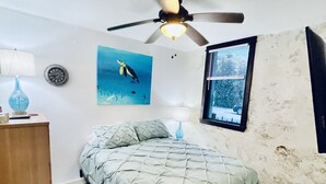 A bedroom with a bed, a ceiling fan, a wall clock, a painting, and a window with blinds. - coral stone 28 day minimum rental  (Key West)