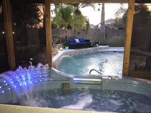 Un jacuzzi con fuente de agua, rodeado por una terraza de madera y una zona de estar exterior azul.