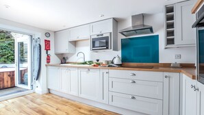 Una cocina moderna con armarios blancos, encimera de madera, microondas integrado y una pared de acento azul.