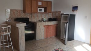 Una cocina con armarios de madera, un microondas, una estufa, un refrigerador y un taburete de bar.