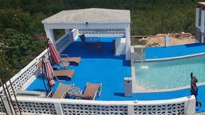Un área de piscina en la azotea con un jacuzzi, sillones de descanso y un espacio de estar cubierto.