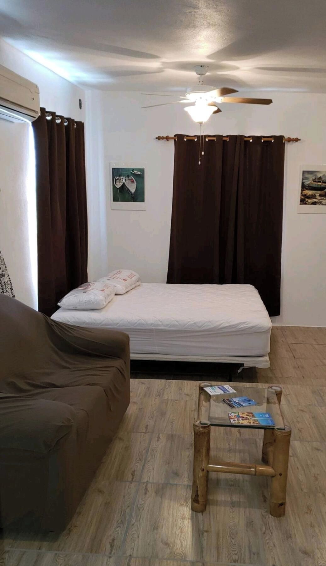 Un dormitorio con cama, una mesita, ventilador de techo y cortinas.