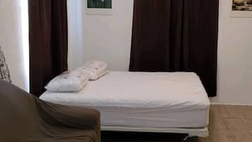 Un dormitorio con cama, una mesita, ventilador de techo y cortinas.
