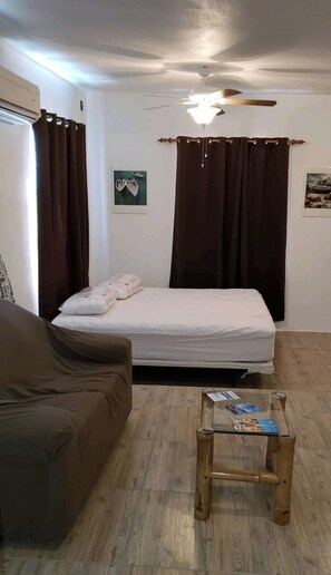 Ein kleiner, gut beleuchteter Raum mit einem Bett, einer Couch, einem Holztisch und einem Deckenventilator.