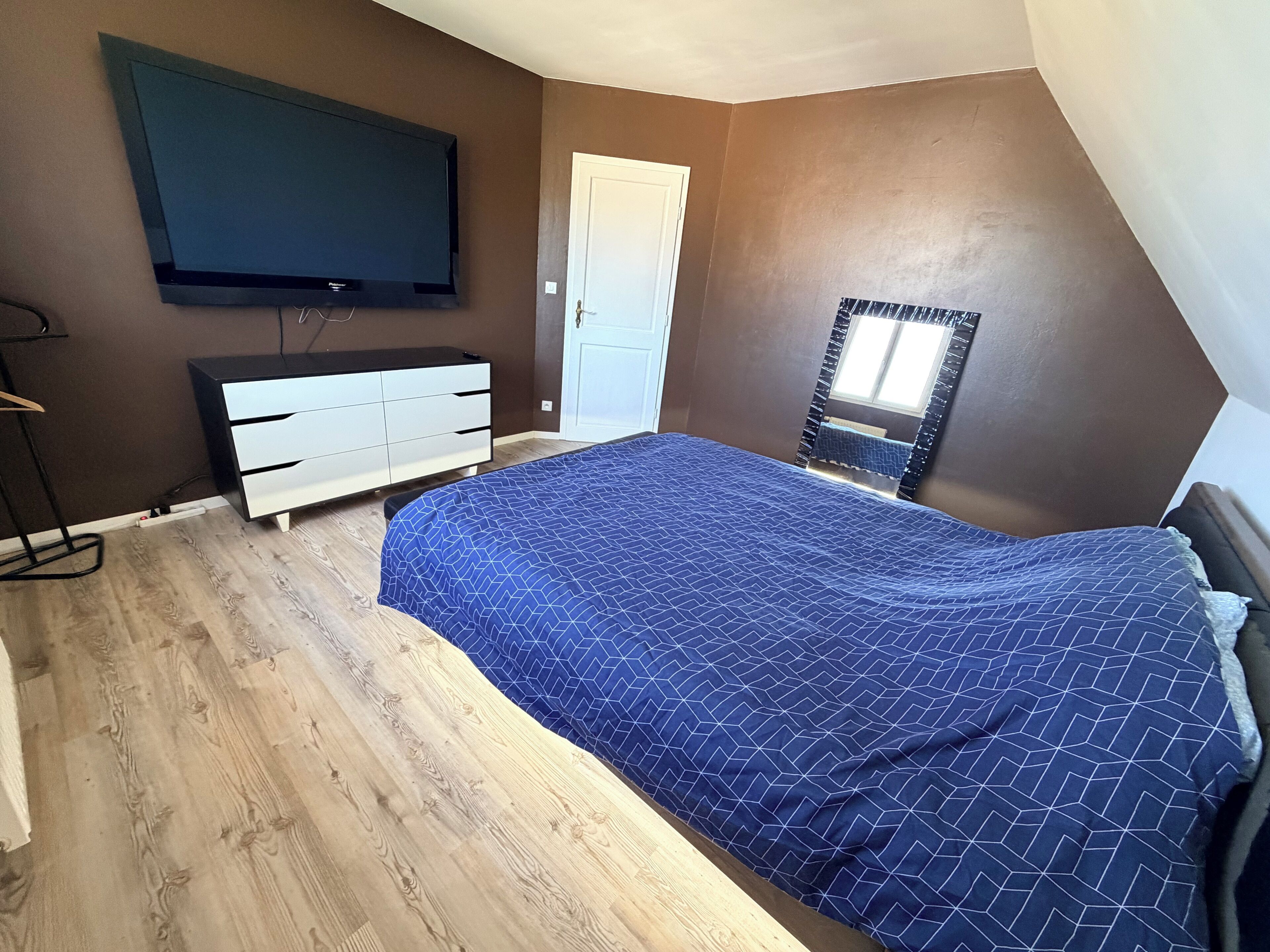 A bedroom with a bed, a dresser, a television mounted on the wall, and a door.