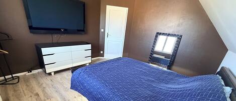 A bedroom with a bed, a dresser, a television mounted on the wall, and a door.