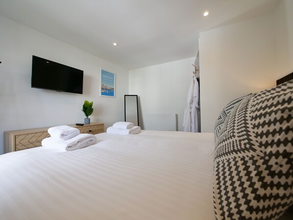 A hotel room with a large bed, a flat-screen TV, a potted plant, a framed picture, and a mirror.