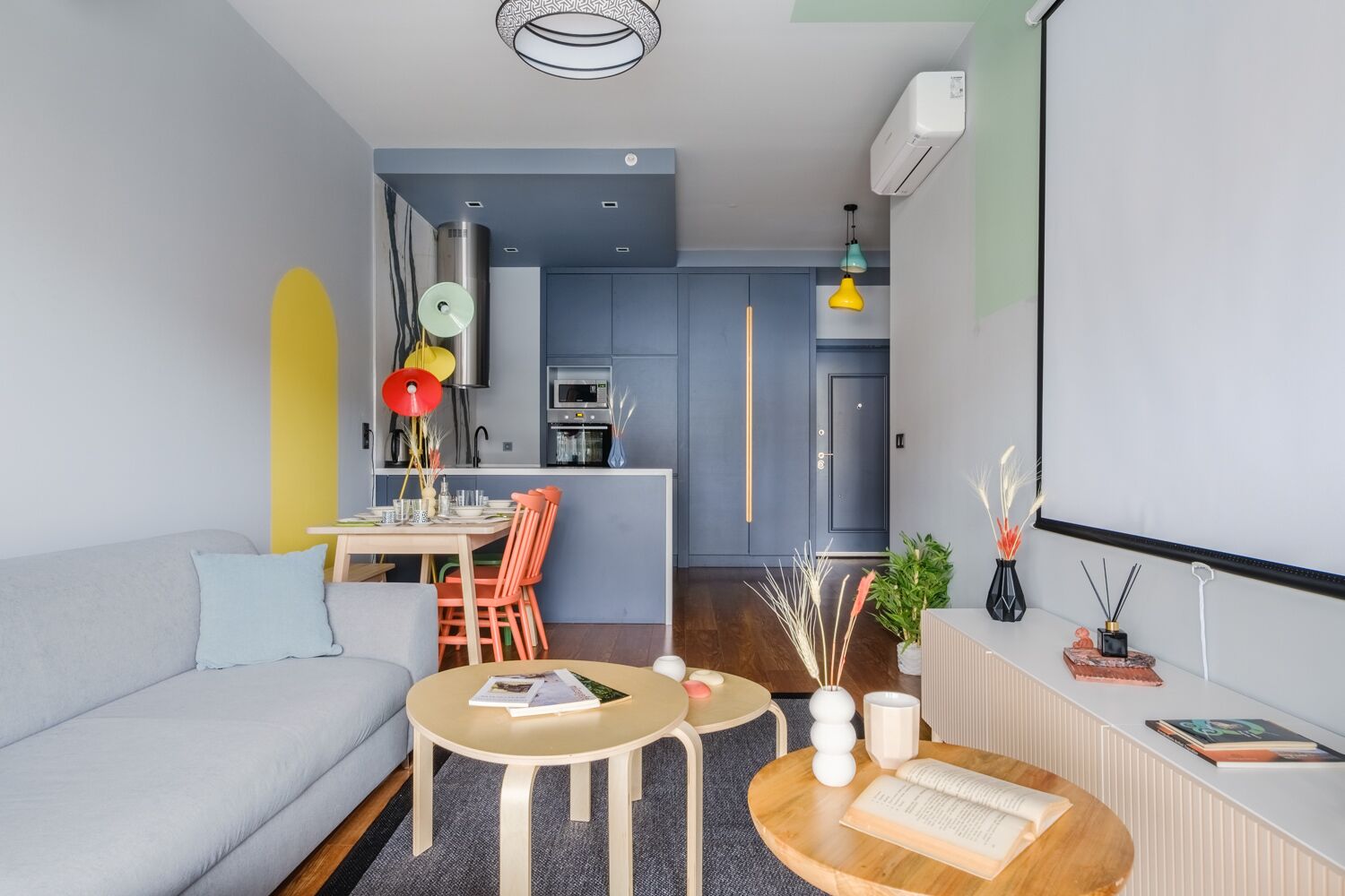 A modern living room with a sofa, coffee table, and dining area. There is a kitchen in the background with a blue door.