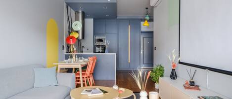 A modern living room with a sofa, coffee table, and dining area. There is a kitchen in the background with a blue door.