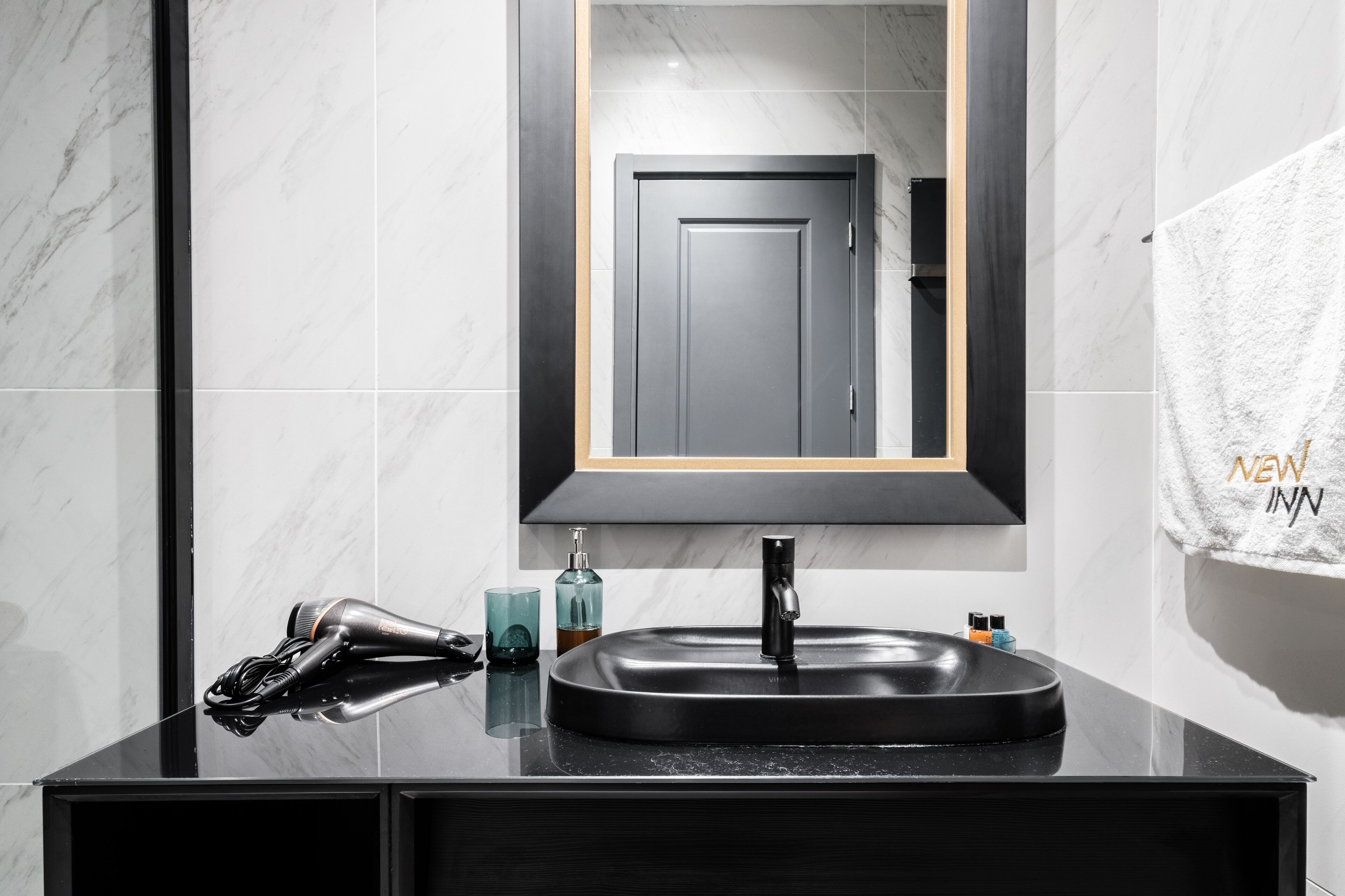 A modern bathroom with a black sink, a hairdryer, and a towel rack.