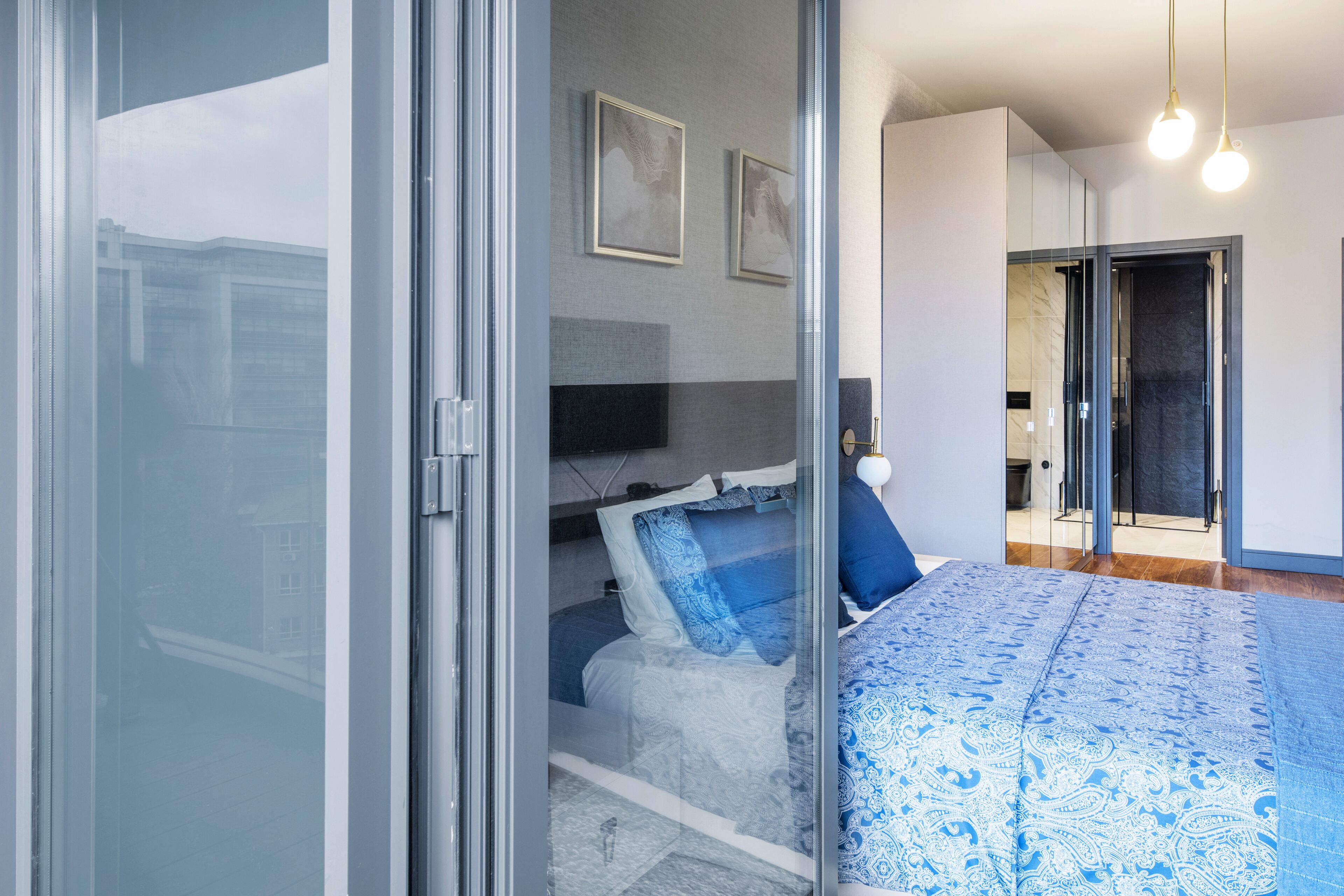 Un dormitorio moderno con puerta de cristal, una cama con ropa de cama azul y un espejo grande.