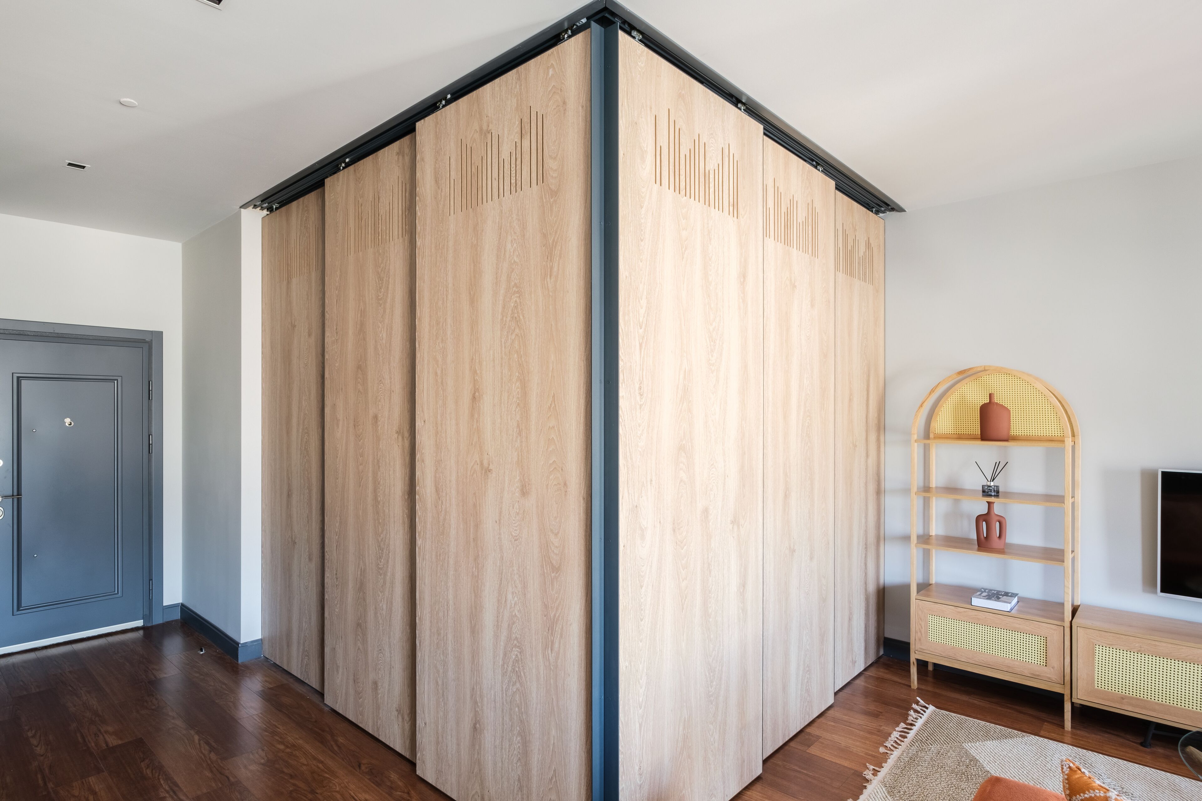 A room with a sliding wooden partition, a wooden shelf unit with a TV, and a dark wooden door.