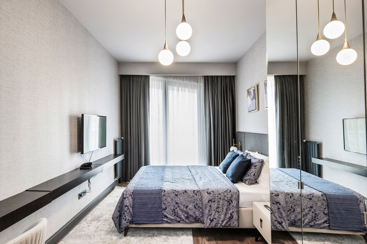 A modern hotel room with a large bed, a TV, and a mirror.