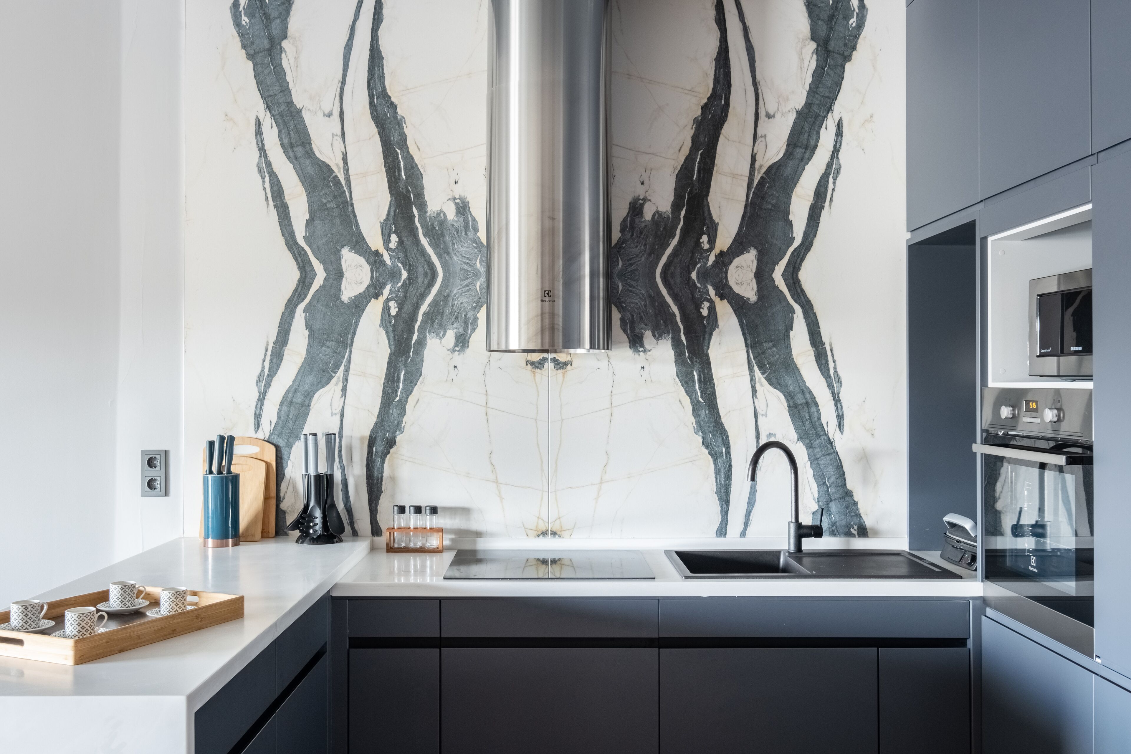 Une cuisine moderne dotée d’un pare-feu en marbre, d’appareils électroménagers en acier inoxydable et d’un design épuré pour les meubles de couleur noire.