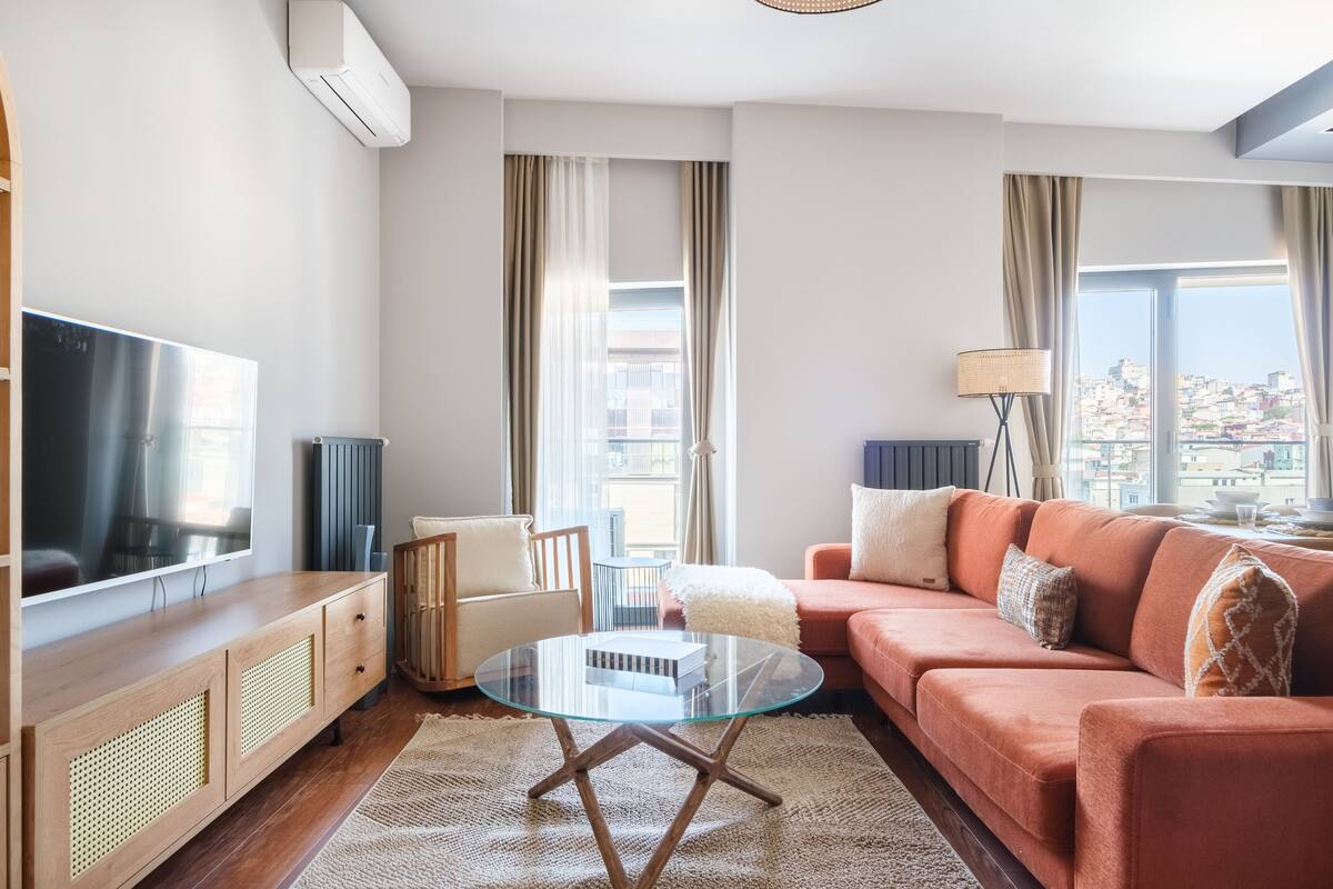 A modern living room with a glass coffee table, a sofa, a TV, and a view of the city.