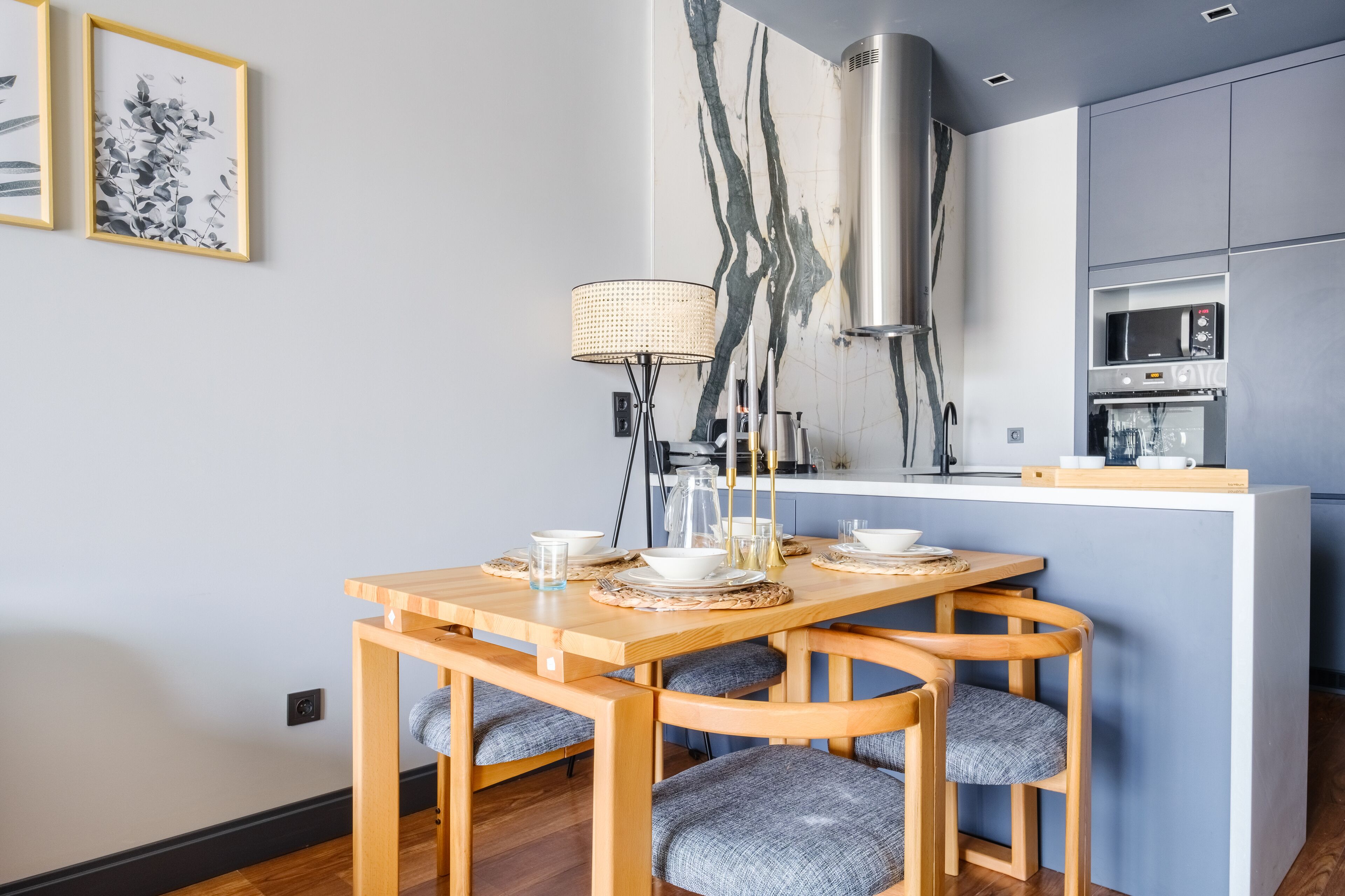 A modern kitchen with a central island, built-in microwave, and oven. There is a dining area with wooden chairs and a table set for two.