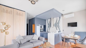 A modern living room with a grey sofa, a dining table with chairs, and a kitchen in the background. - Benesta Residence By Newinn (Istanbul)