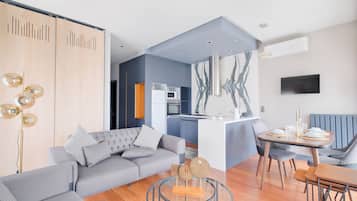 Een moderne woonkamer met een grijze bank, een eettafel met stoelen en een keuken op de achtergrond.
