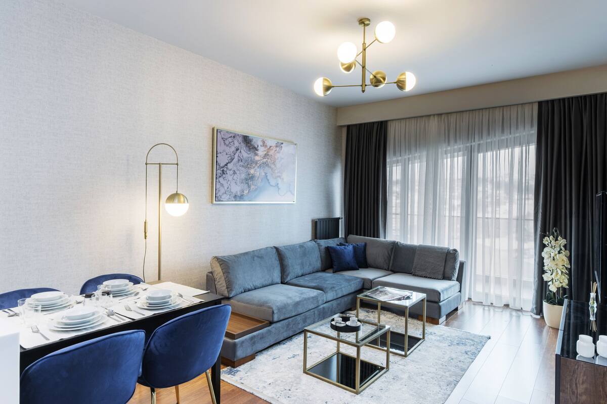 A modern living room with a sectional sofa, a dining table set for four, and a large window with curtains.