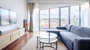 A modern living room with a large window, a grey sofa, a glass coffee table, and a TV on a wooden cabinet. - Benesta Residence By Newinn (Istanbul)