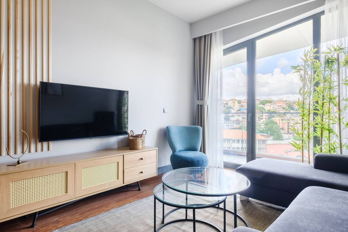 A modern living room with a flat-screen TV, a blue armchair, a glass coffee table, and a sofa.