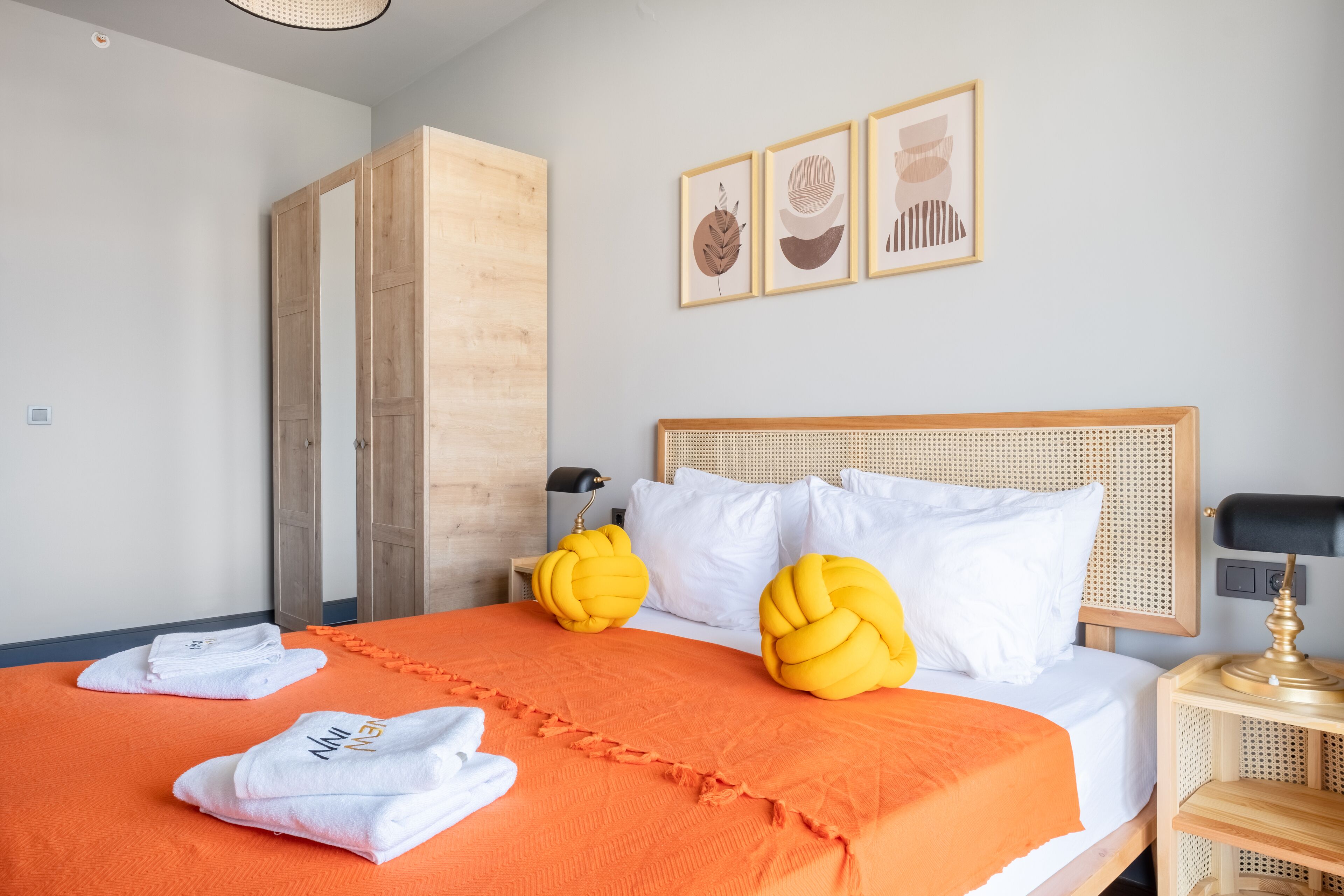 A hotel room with a bed, wooden wardrobe, and artwork on the wall.