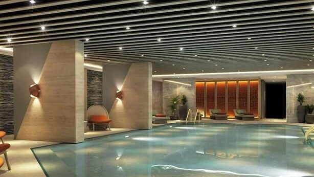 A modern indoor swimming pool with a geometric ceiling design, lounge seating, and a stone wall backdrop. - Benesta Residence By Newinn (Istanbul)