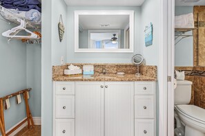 A bathroom with a granite countertop, white cabinets, a mirror, and a towel rack.