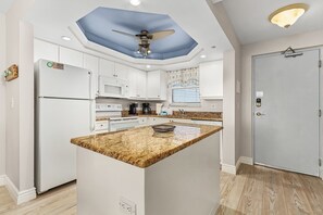 Una cocina moderna con armarios blancos, encimera de granito y ventilador de techo.