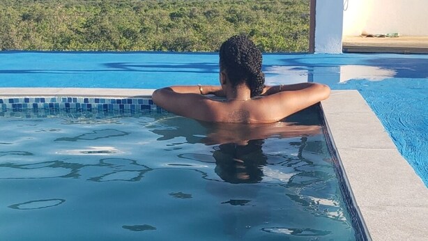 A person relaxing in a swimming pool with a view of mountains and greenery in the background.