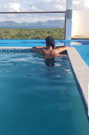 A person relaxing in a swimming pool with a view of mountains and greenery in the background. - OUR STUDIO APARTMENTS COMES EQUIPPED WITH ALL ESSENTIAL NEED (THE VALLEY)