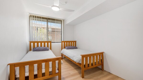A room with two wooden bunk beds, a ceiling fan, and a window with blinds.