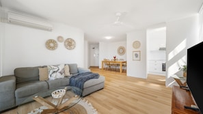 A modern living room with a grey sofa, a glass coffee table, and a dining area with a wooden table and chairs.