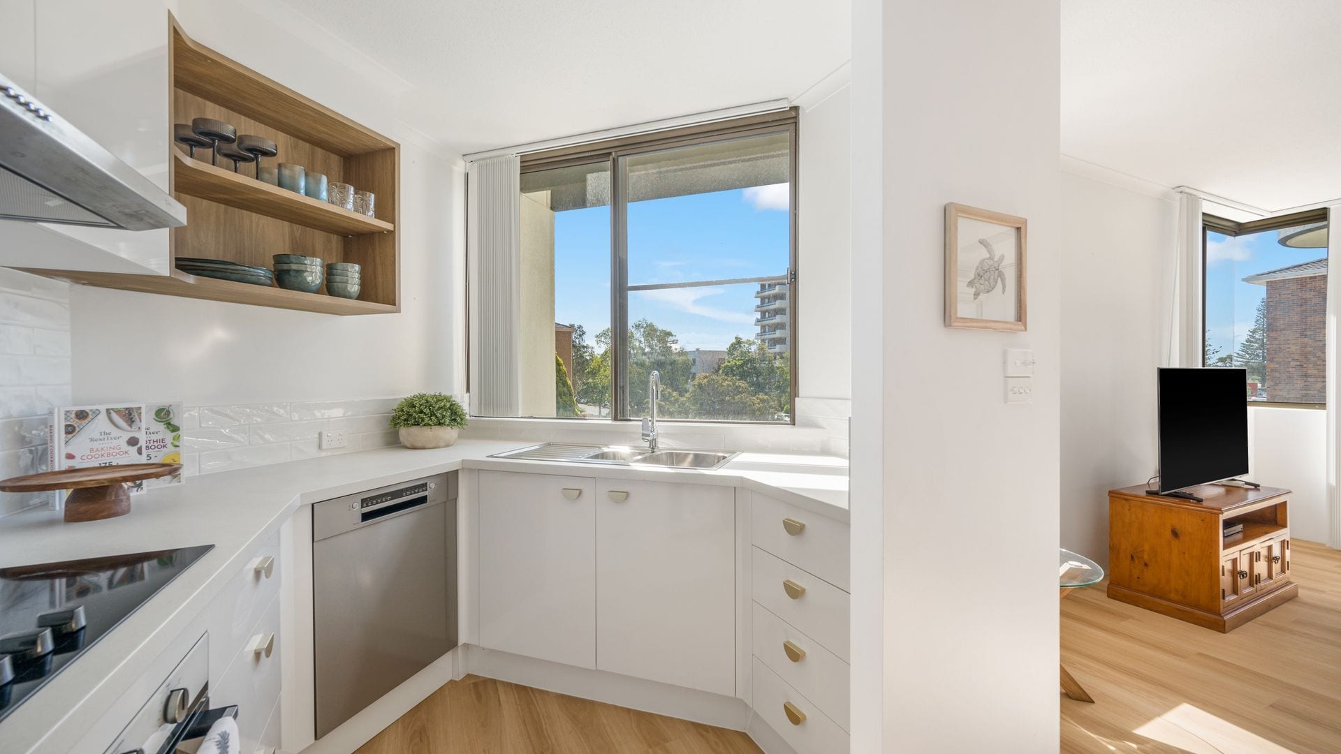 Eine moderne Küche mit weißen Schränken, einem eingebauten Geschirrspüler, einem Fenster mit Ausblick und einem Holzschrank mit Geschirr.
