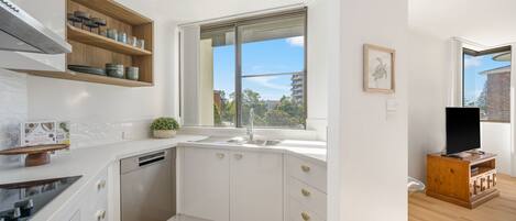Eine moderne Küche mit weißen Schränken, einem eingebauten Geschirrspüler, einem Fenster mit Ausblick und einem Holzschrank mit Geschirr.