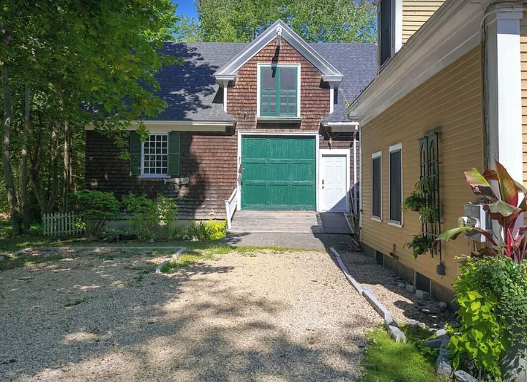 A residential property with a gravel driveway, a green garage door, and a small front yard with plants.