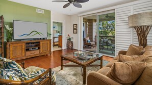 A spacious living room with a flat-screen TV, wooden furniture, and a glass coffee table. - Pili Mai at Poipu #15J By Parrish Kauai - great central Poipu location, walkabl (Koloa)
