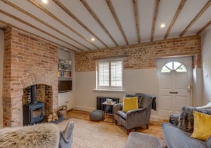 Cozy living room with a brick fireplace, comfortable seating area, and a bookshelf.