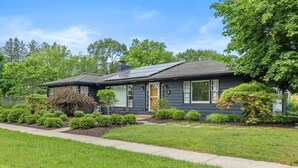 A two-story house with a dark exterior, a front porch, and a well-maintained lawn. - Captains Cove, hot tub walk to Douglas! (Douglas)