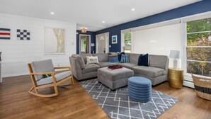 A modern living room with a grey sofa set, a wooden rocking chair, and a patterned rug. - Captains Cove, hot tub walk to Douglas! (Douglas)