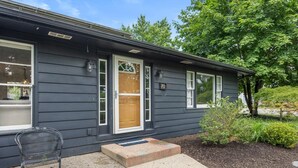 A single-story building with a dark exterior, a front door, and a small porch area with a bench. - Captains Cove, hot tub walk to Douglas! (Douglas)
