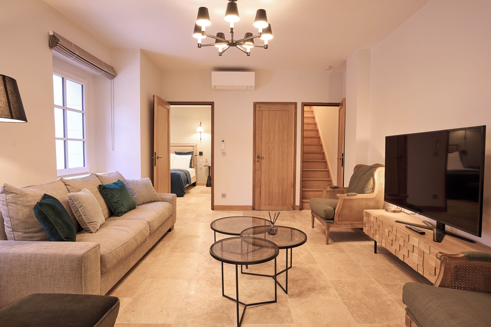A living room with a sofa, two round tables, a TV, and a staircase leading to a bedroom.
