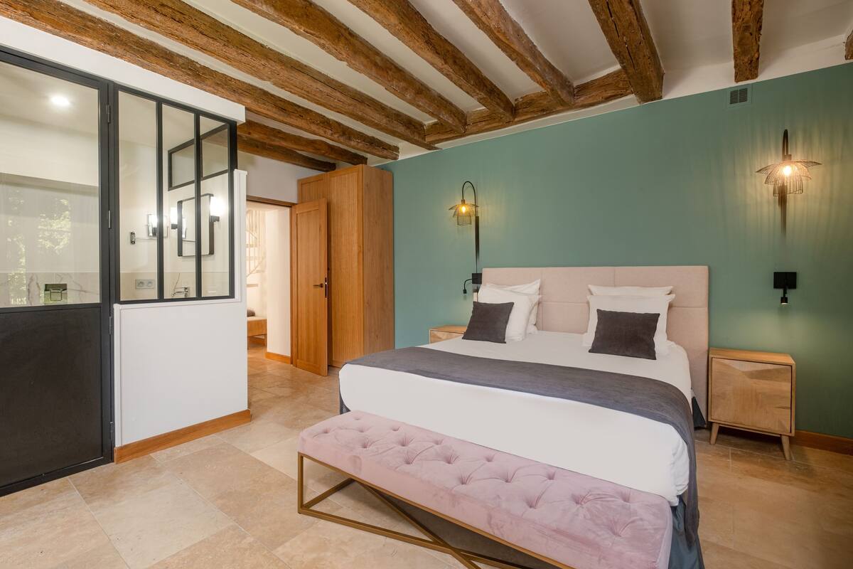 Ein Schlafzimmer mit Bett, Bank, Holzbalken an der Decke und einer grünen Wand.