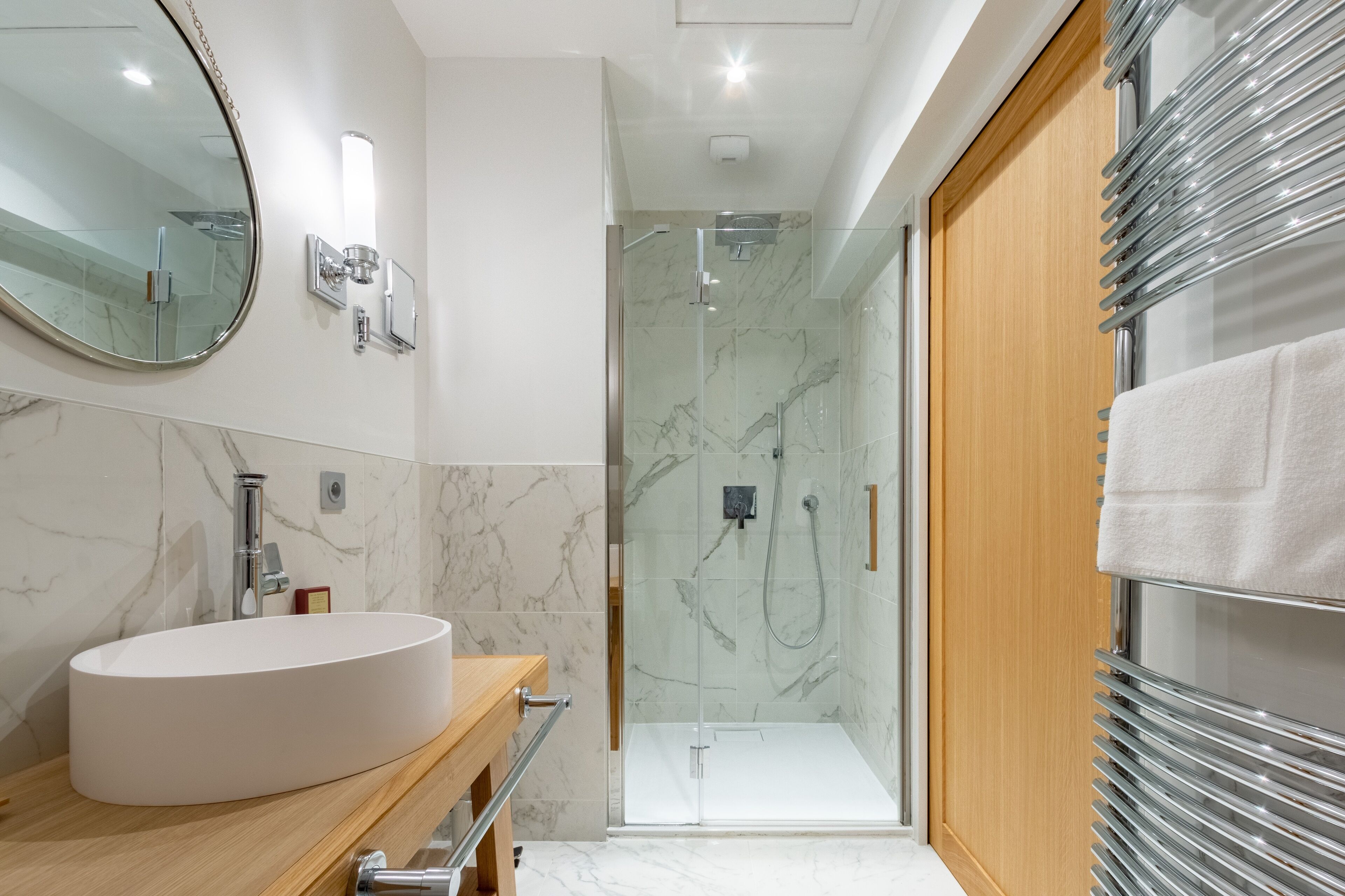 A modern bathroom with a large oval sink, a glass-enclosed shower, and a wooden vanity.