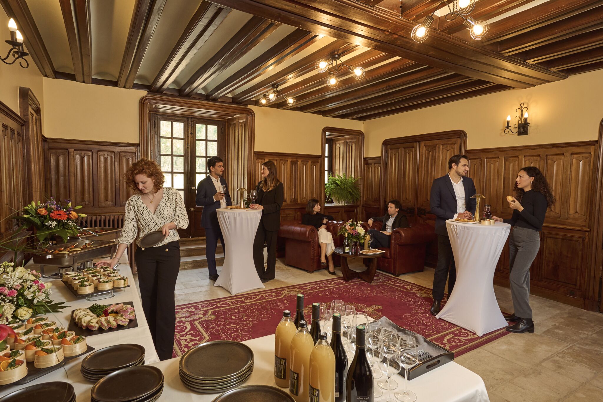 A formal event with tables set for dining, a buffet with various food items, and a selection of wine bottles.