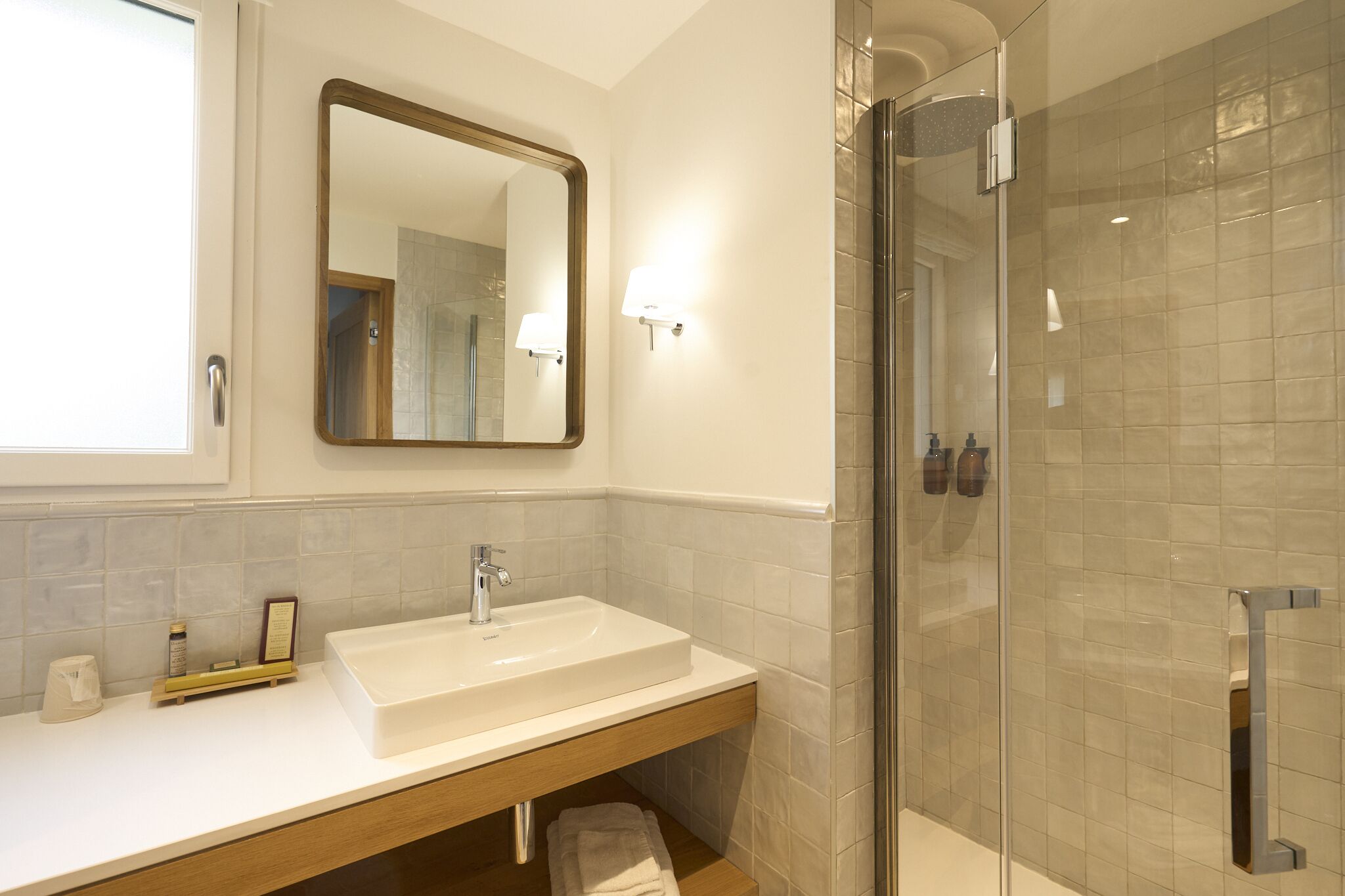 Un baño moderno con un espejo grande, un lavamanos blanco y una cabina de ducha con paredes de vidrio.
